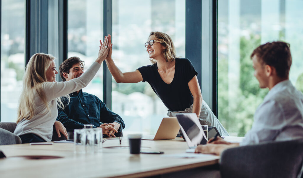 Female professional giving a high five to her colleague in conference room. Group of colleagues celebrating success in a meeting.